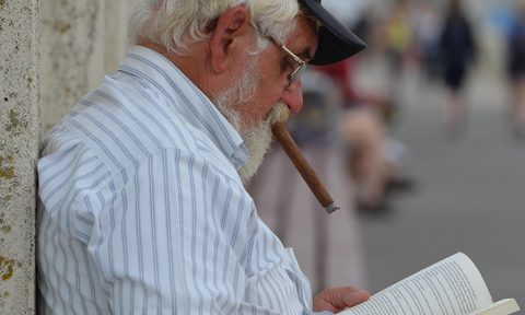 an old man smoking a cigar while reading a book