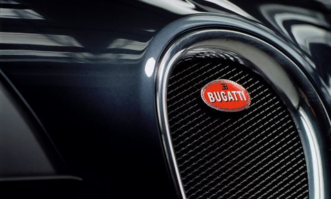 Frontal photo of a dark grey Bugatti Veyron with a red Bugatti badge.