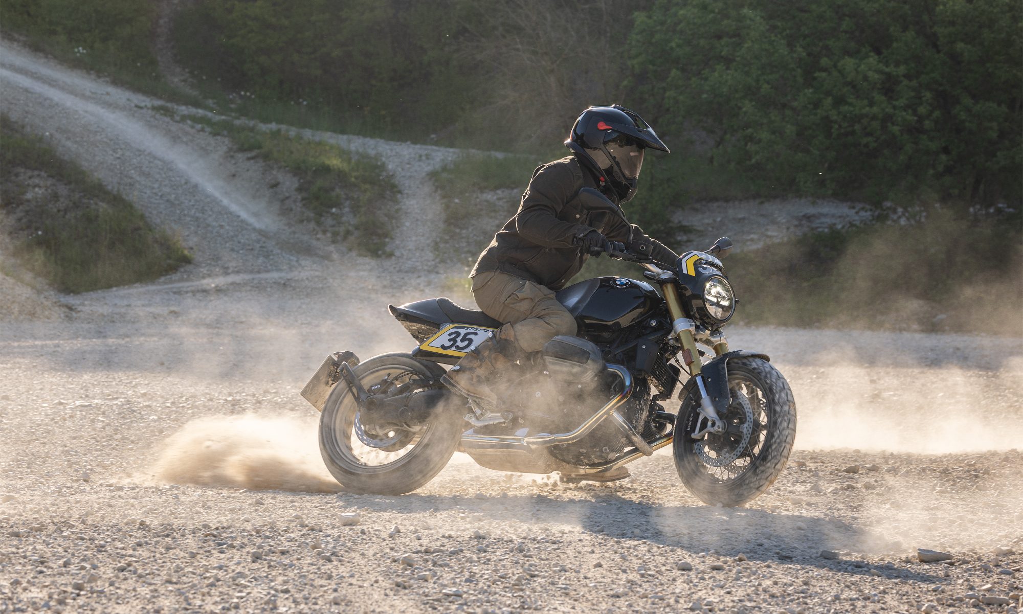 Rider on 2026 BMW R 12 NineT with Tracker package scrambling on gravel.
