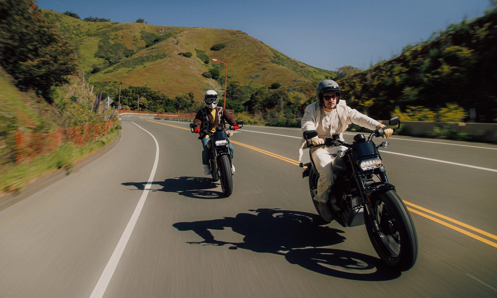 Two riders on LiveWire S2 Del Mars on a highway with rolling hills in the background.