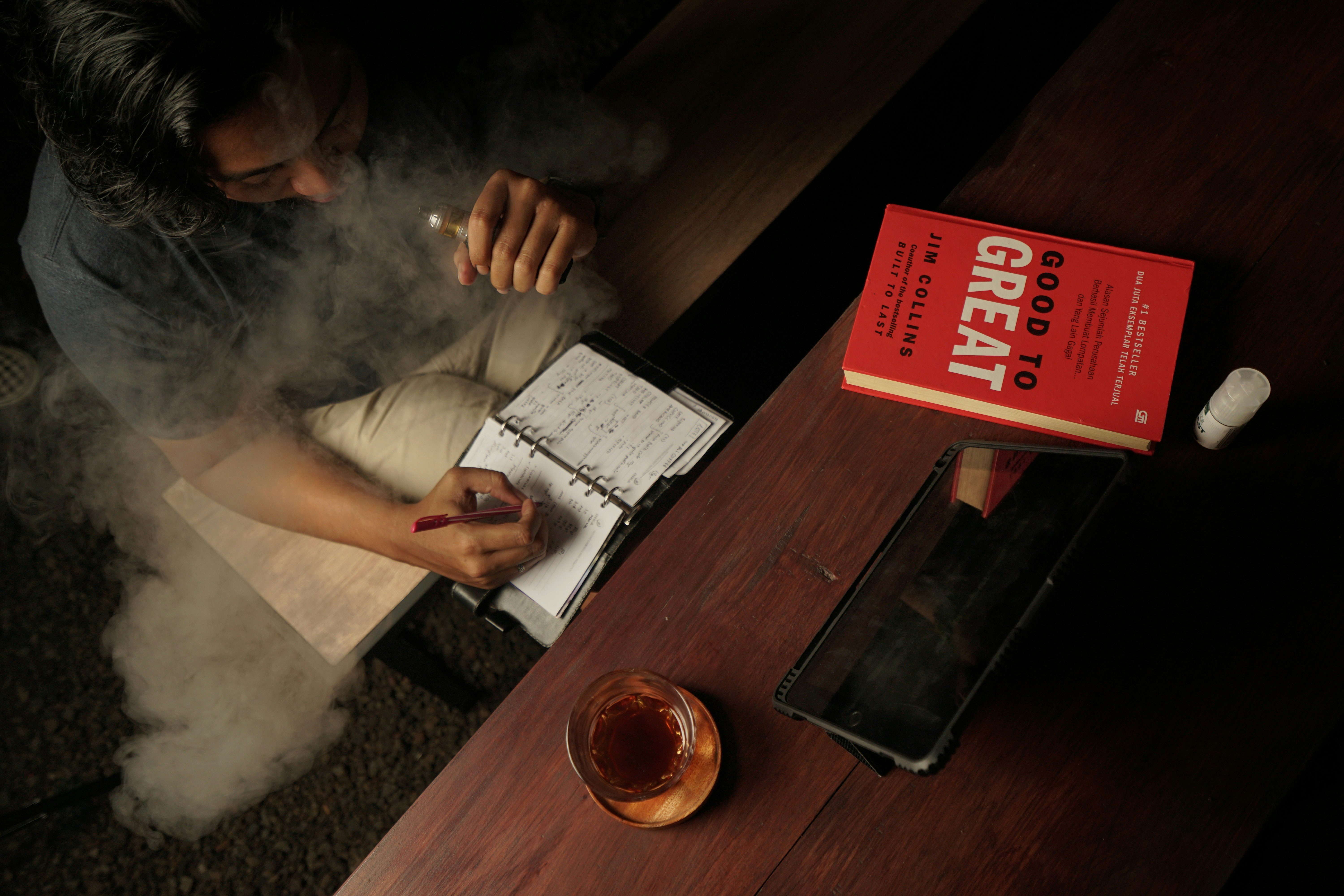 man writing notes while smoking