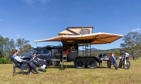 Two men sitting outside near a Hardkorr Campers HKC Xplorer Toy Hauler off-road travel trailer.
