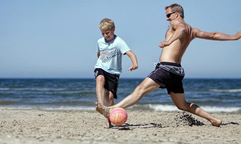 man playing with kid running football beach