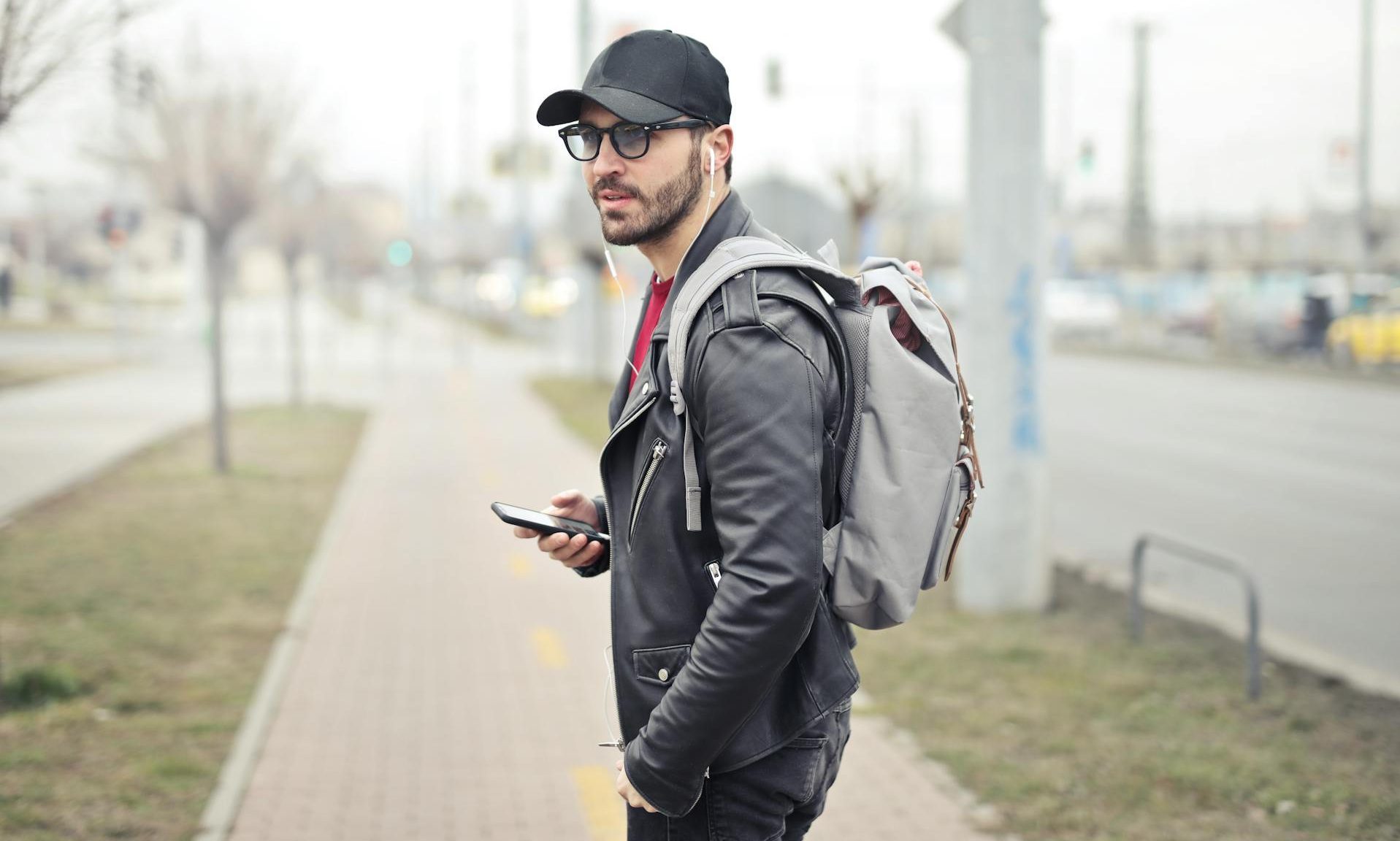 man walking in city holding phone headphones