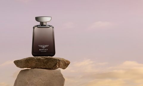 Bentley Become Zenith fragrance bottle balanced on a flat rock on top of a tall rock with sky and clouds in the background.