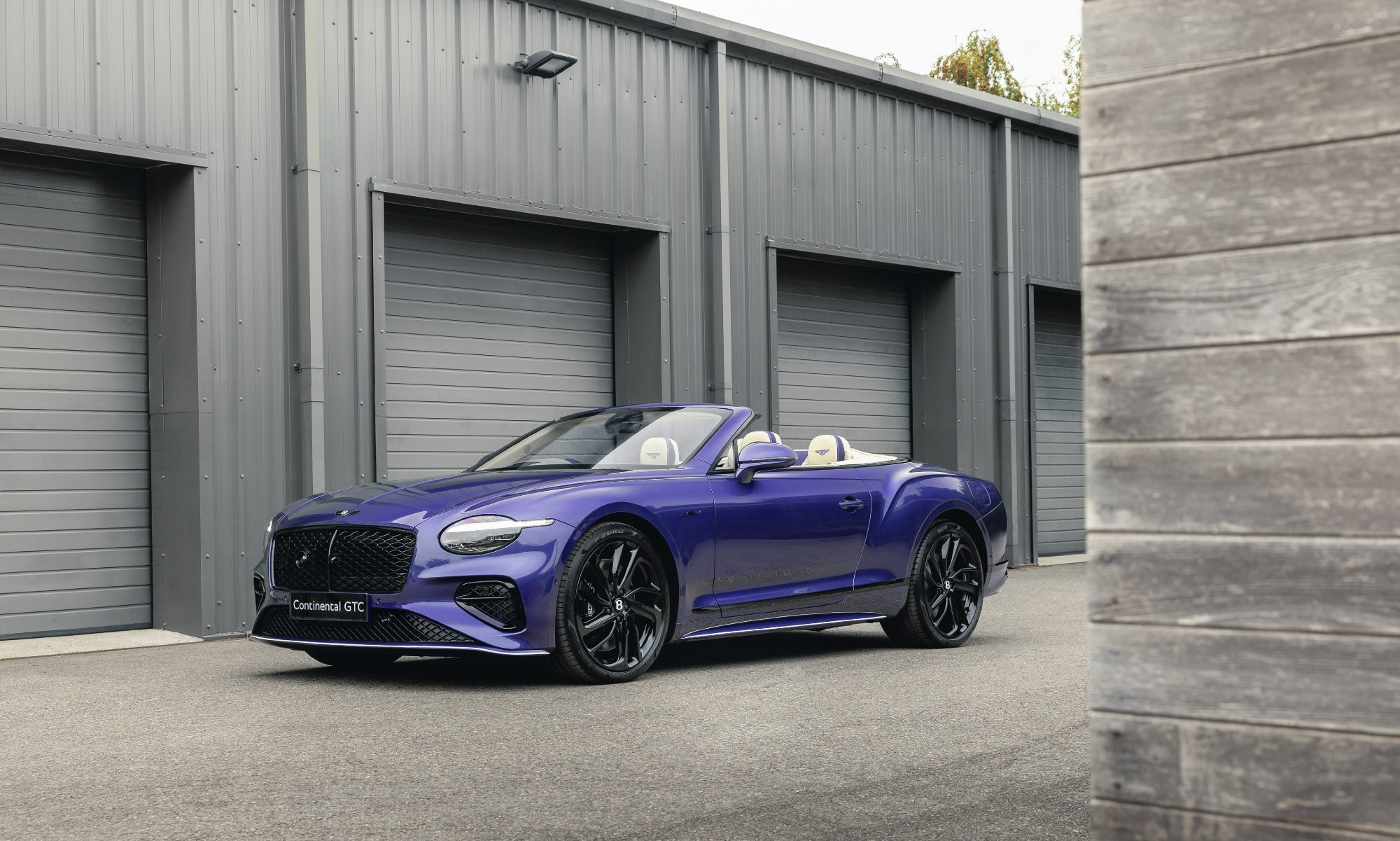 Bentley Continental GTC Speed in Violette finish with top down parked in front of a garage left front three quarter view.