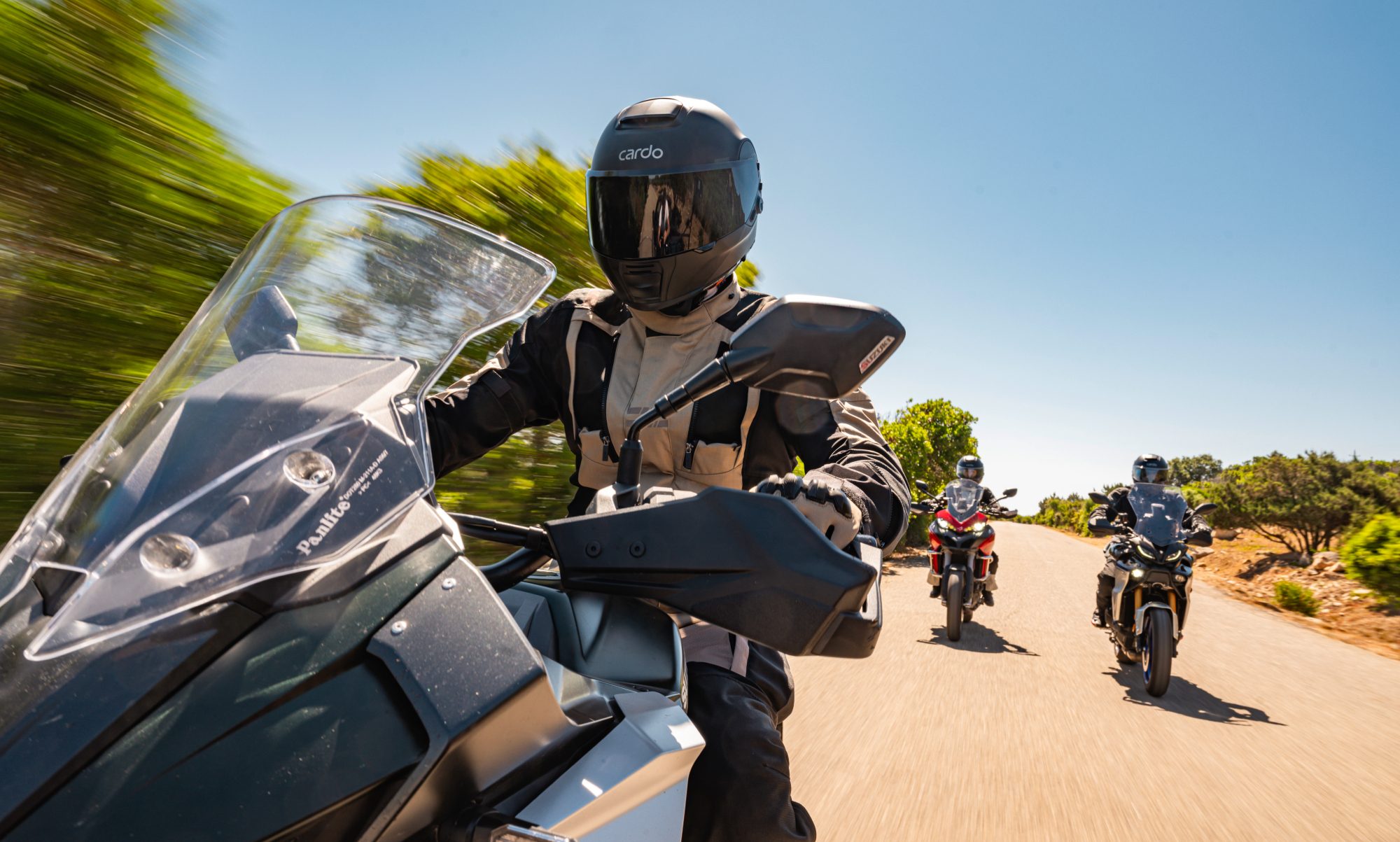 Three motorcycle riders on a country mountain road wearing Cardo Beyond helmets.