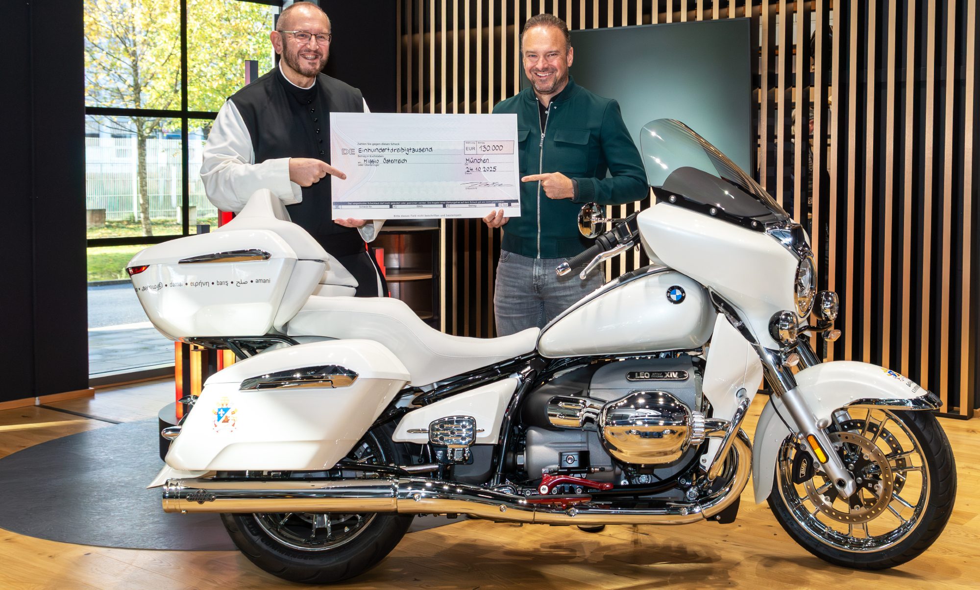 Two people holding the check that paid for the Pope's BMW R 18 Transcontinental.