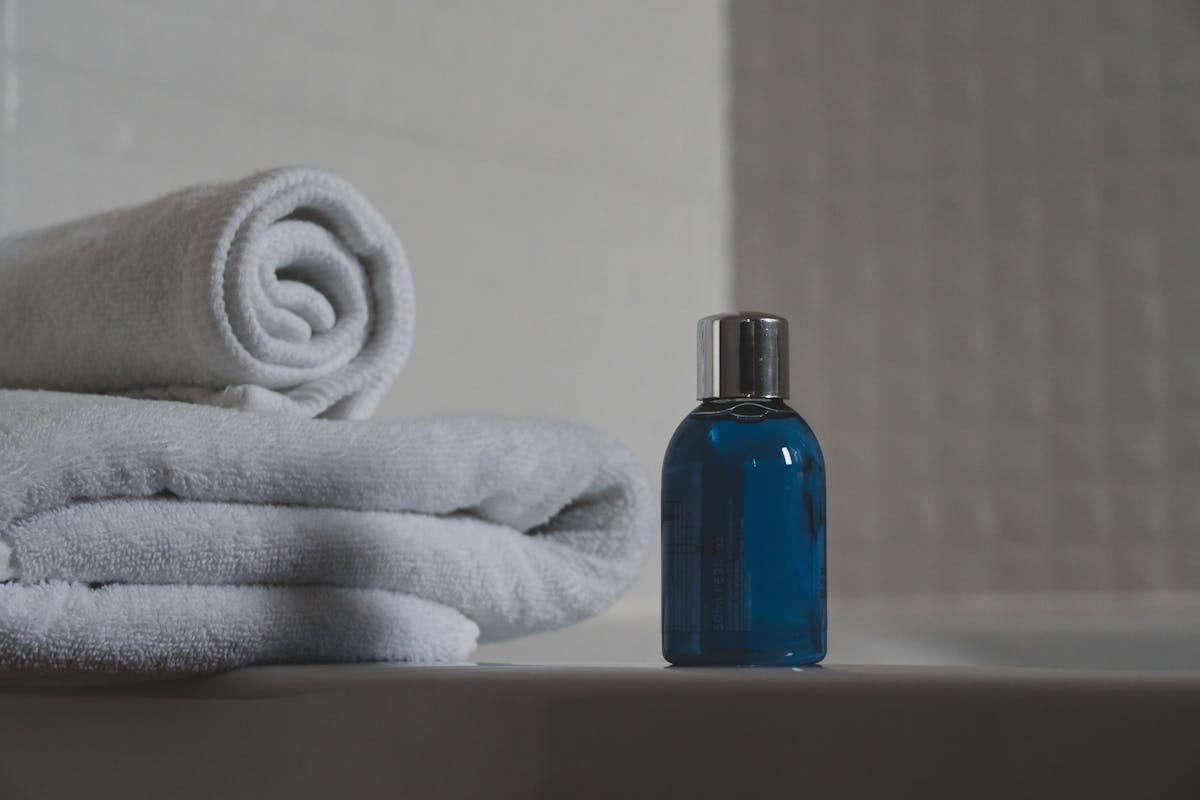 Blue shampoo bottle on white bath with white towel piled next to it 
