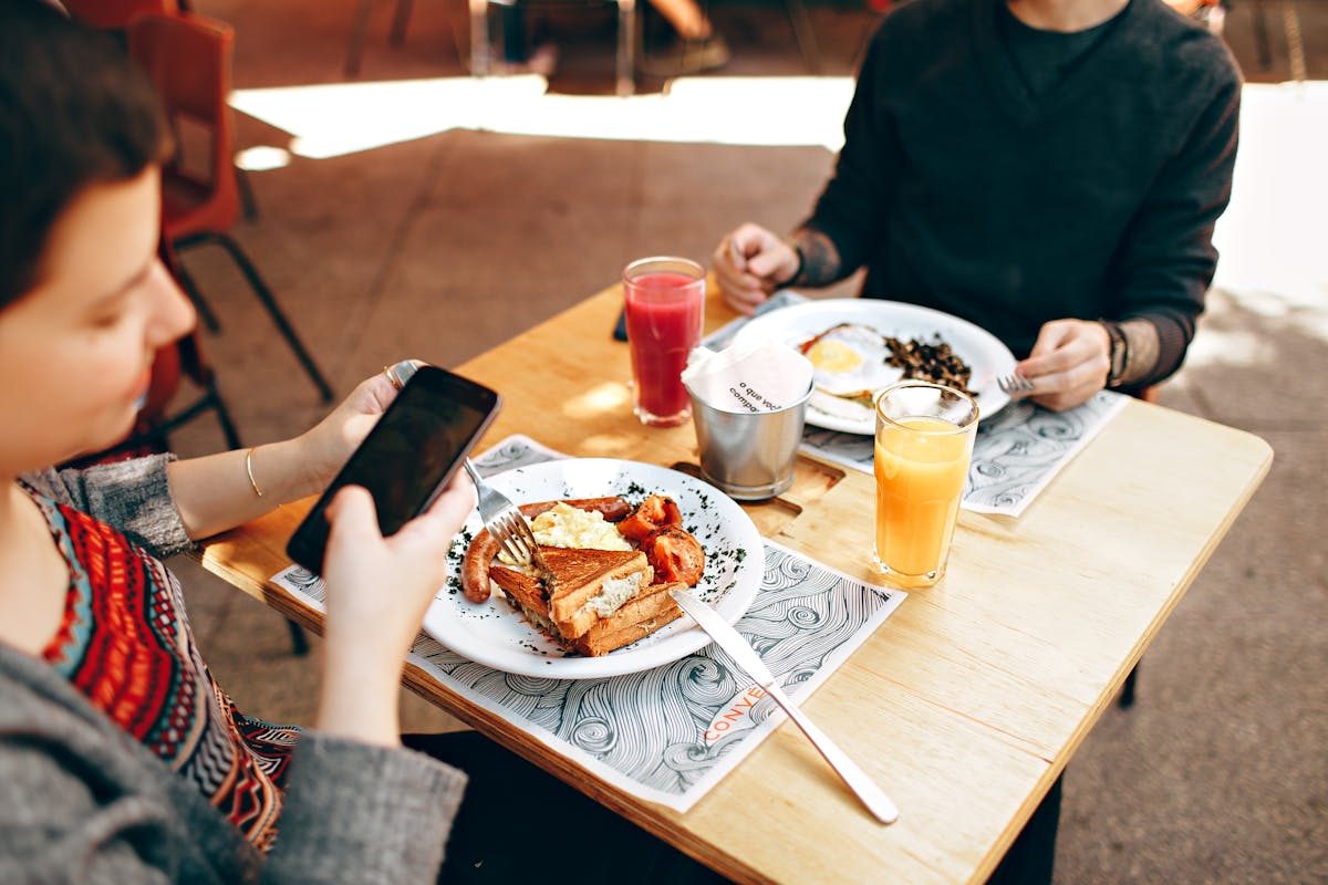 two young men eating outside taking photos of food on phone