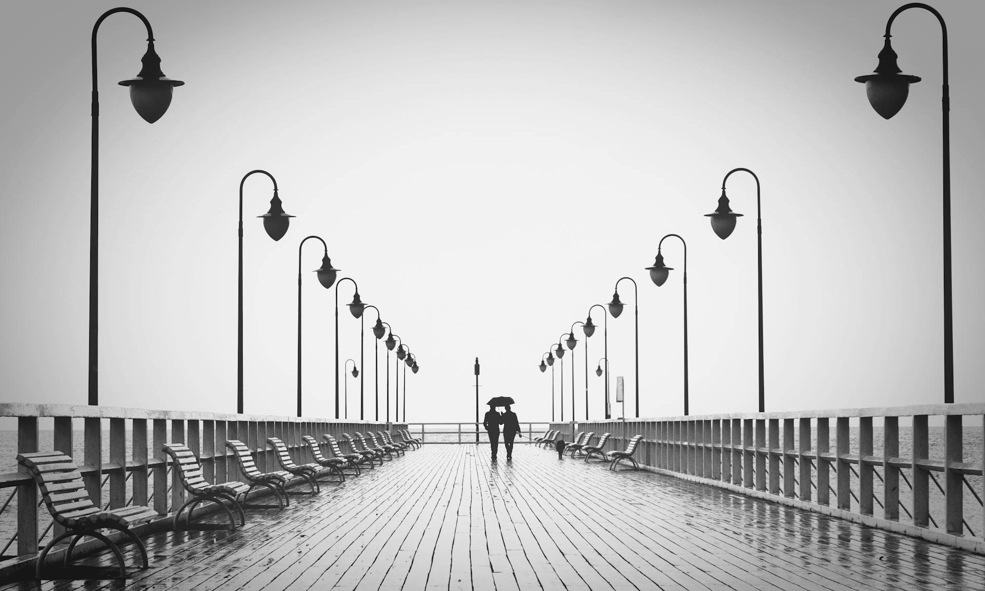 two people holding umbrella walking on pier