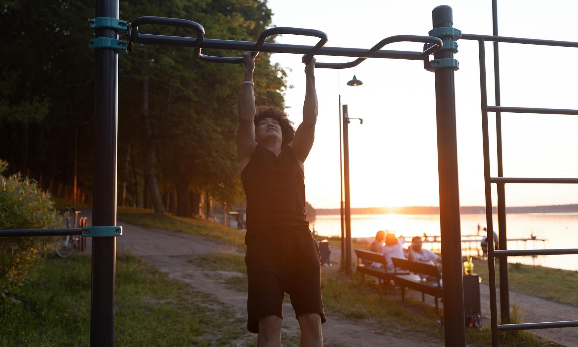 man exercising pull up bars outside sunset