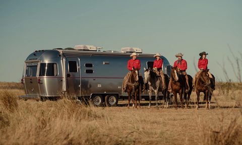 An Airstream Stetson x 6666 Special Edition Travel Trailer parked in a field with four cowboys in the foreground.