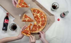 people reaching for pizza with soda on table