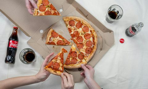 people reaching for pizza with soda on table