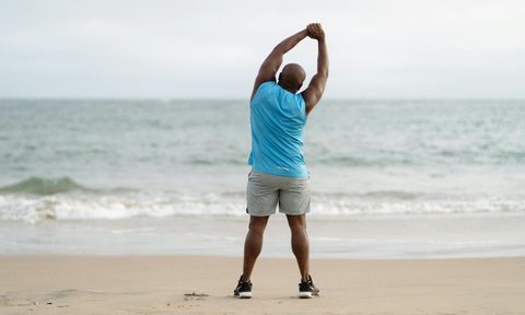 man stretching and exercising by ocean on beach