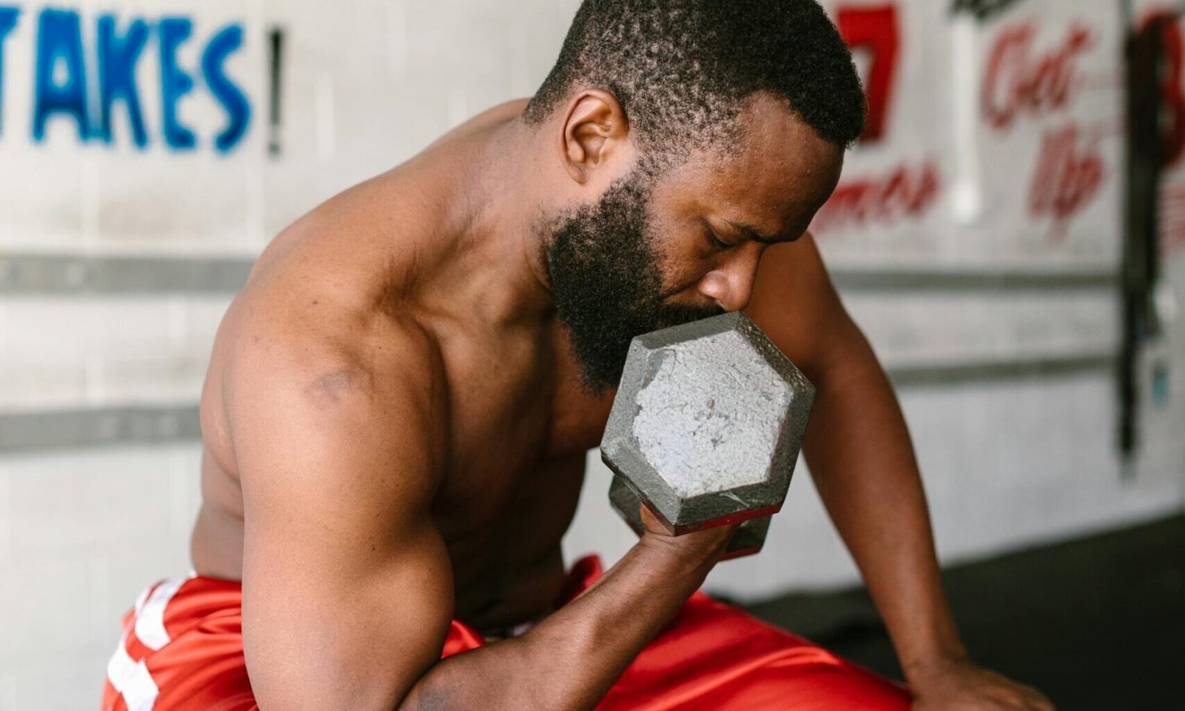 man sitting on bench in gym lifting weights dumbbell bicep curl