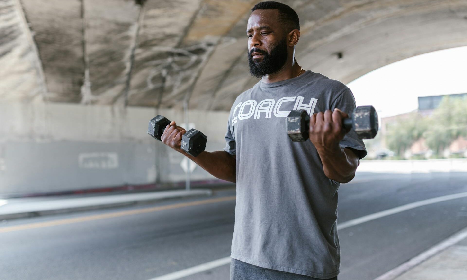 man lifting weights dumbbells outside