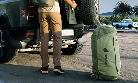 Man standing outside an SUV with Deuter's Duffel Pro Roller 90 adventure bag.