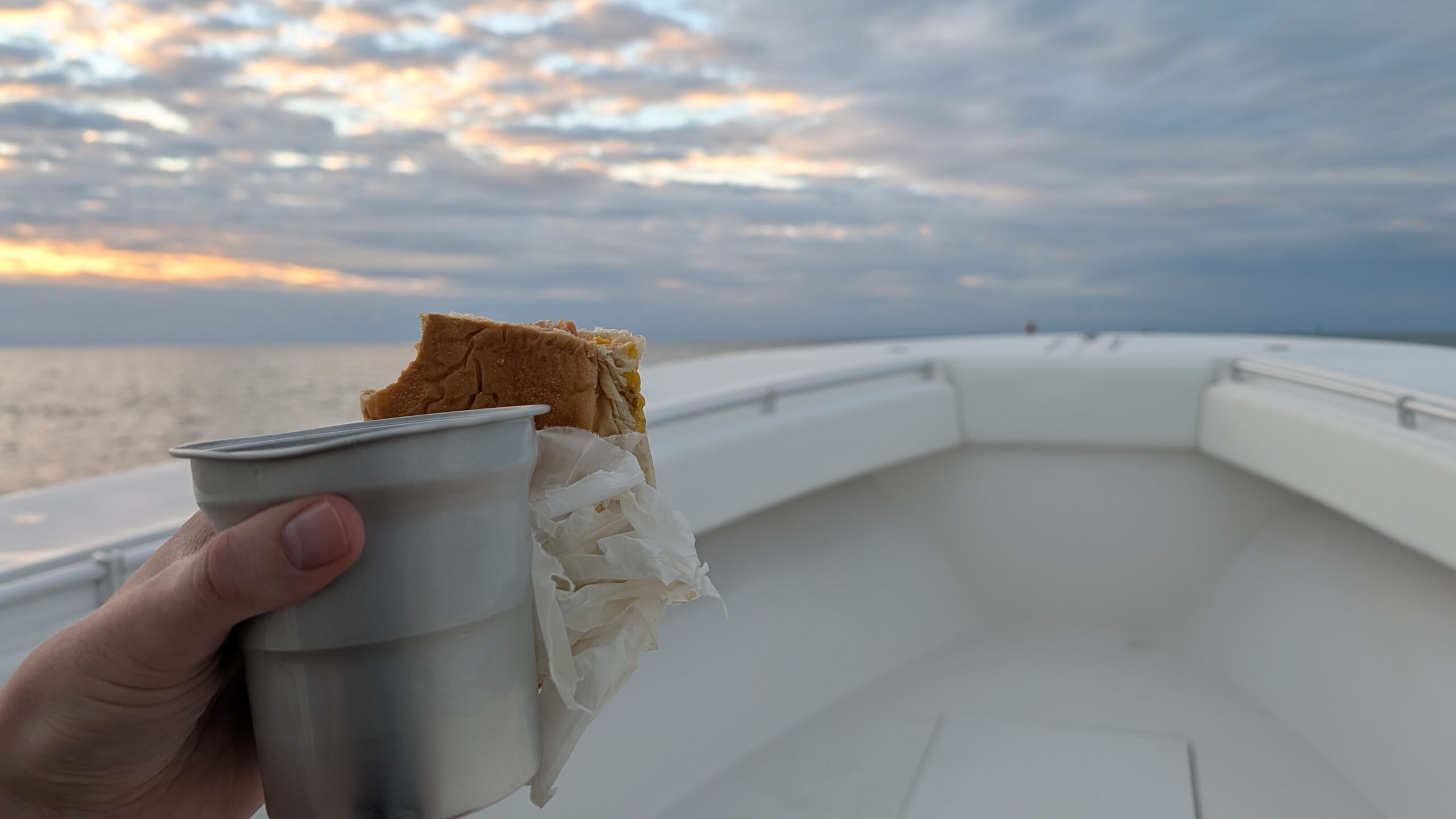 A breakfast sandwich and coffee with the bow of a boat and the horizon in front of it