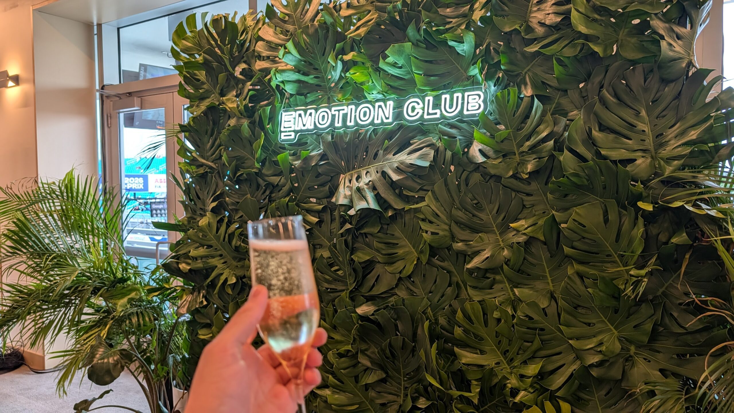 Holding a glass full of champagne in front of the Emotion Club logo