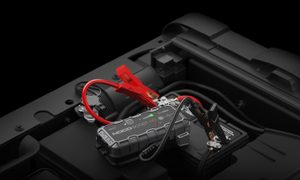 A Noco GB70 portable automotive jump starter hooked up to a vehicle battery.