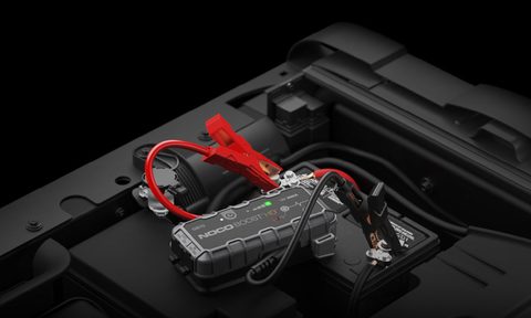 A Noco GB70 portable automotive jump starter hooked up to a vehicle battery.