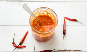 Homemade hot sauce in a jar with small red chili peppers on the side.