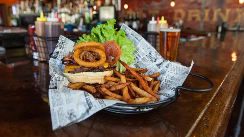 Burger topped with onion rings, lettuce, and tomato with a side of crispy fries.