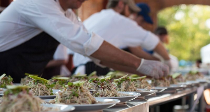 chef with gloves on plating a row of food.