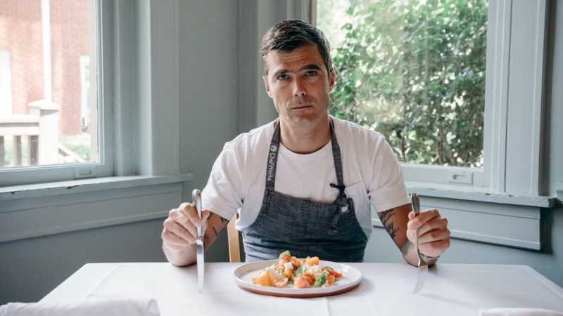 hugh acheson celebrity chef with fork and knife in hand and dinner plate at table