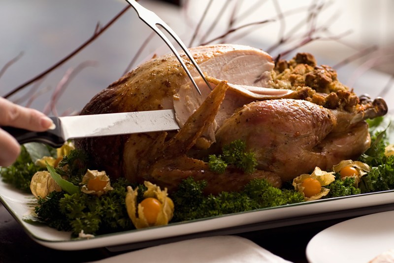 hand holding a knife and a serving fork carving a turkey.