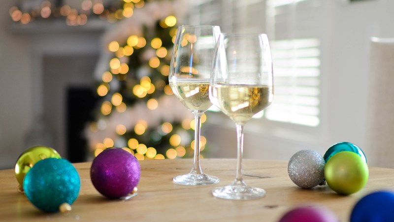 Two glasses of wine and Christmas balls on a table in a room with Christmas tree.