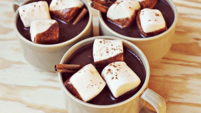 Three cups of Aztec hot chocolate with marshmallows and cinnamon sticks on a table.