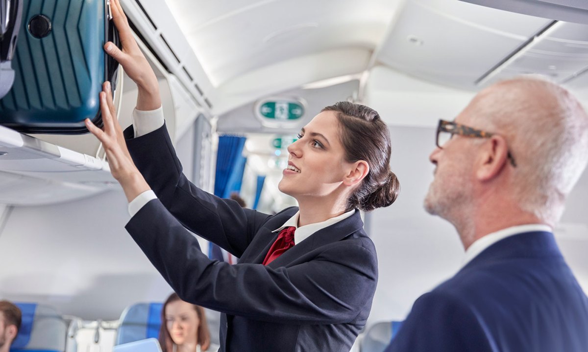 Flight attendant helping businessman place luggage in overhead compartment on airplane