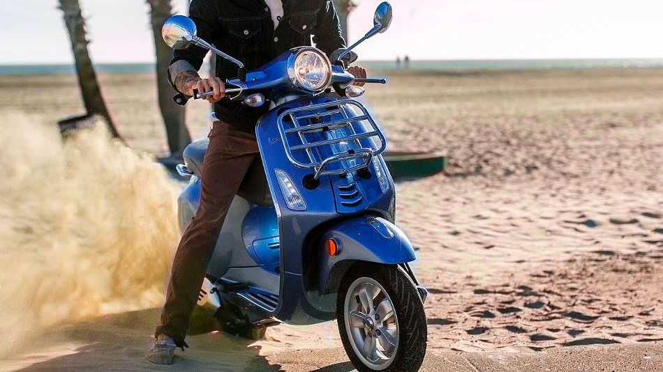 Close up of vespa gtv on the sand throwing up sand from the rear tire.