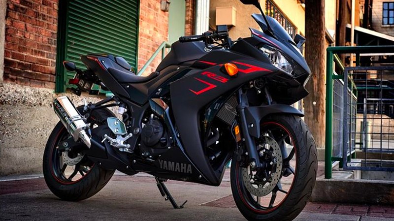 Front end angle of Yamaha R3 parked in front of brick buildings.