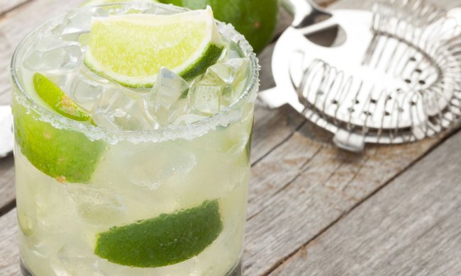 Classic margarita cocktail with salty rim on wooden table with limes and drink utensils