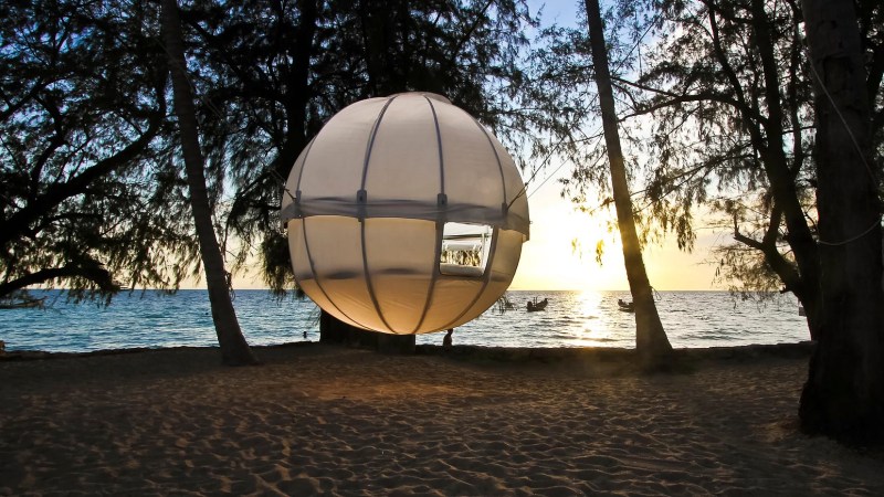 Cocoon Tree luxury glamping shelter suspended between trees near a beach.