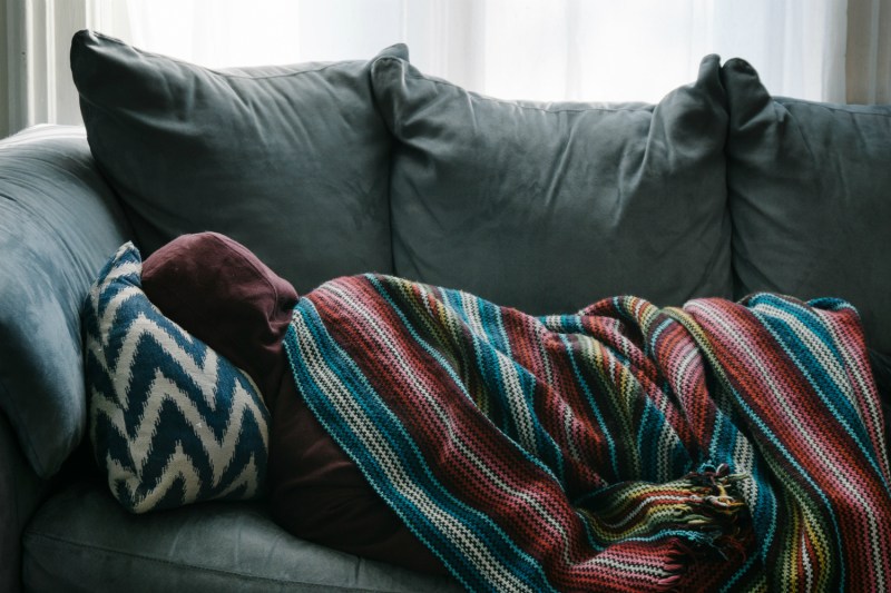 A person curled up sick on a couch.