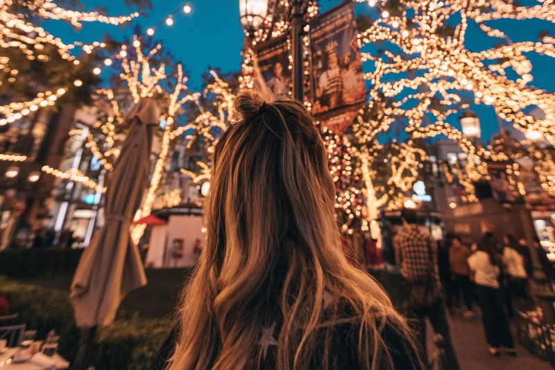 Woman looking up at lights strung in a Christmas market at night.