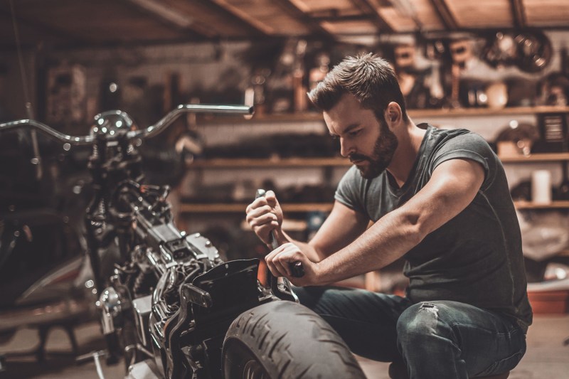 Man repairing his motorcycle in his garage with a set of hand tools.