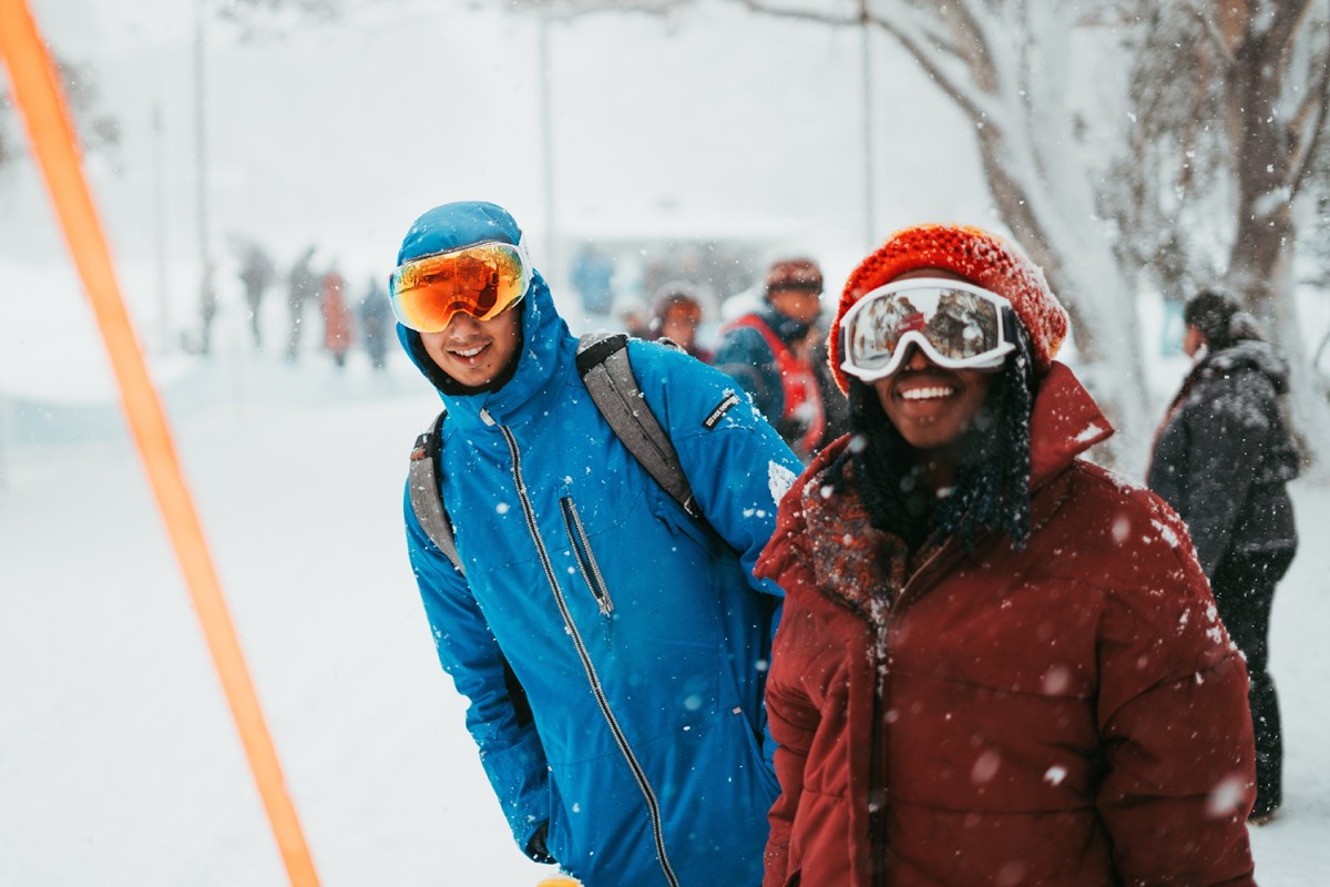 Two characters in ski gear face the camera as snow falls on them.