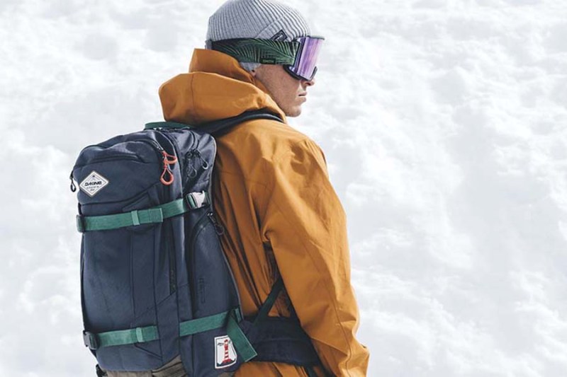 Snowboarding man wearing a Dakine Team Mission Pro 32L Backpack.