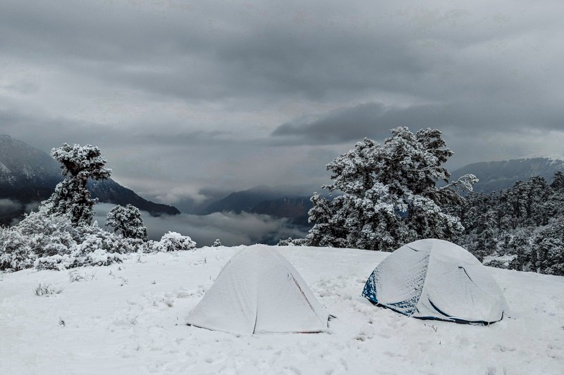 Two camping tents covered in snow on a mountain in winter.