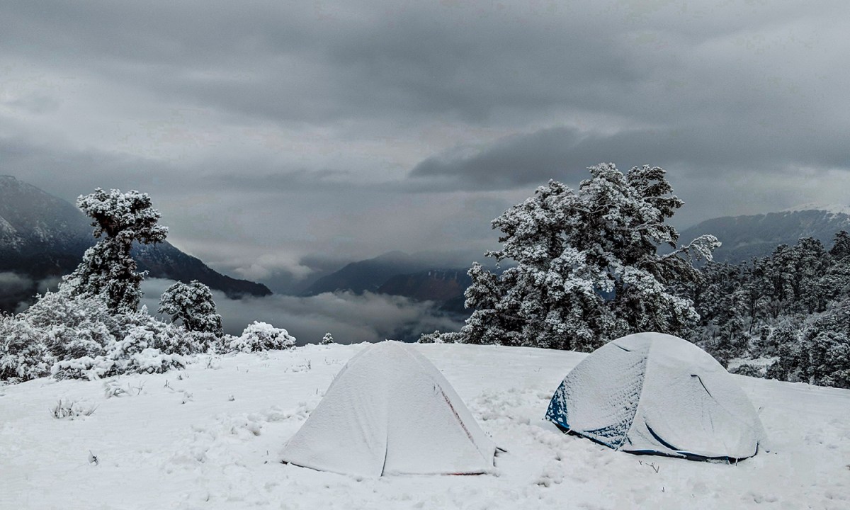 Two camping tents covered in snow on a mountain in winter.