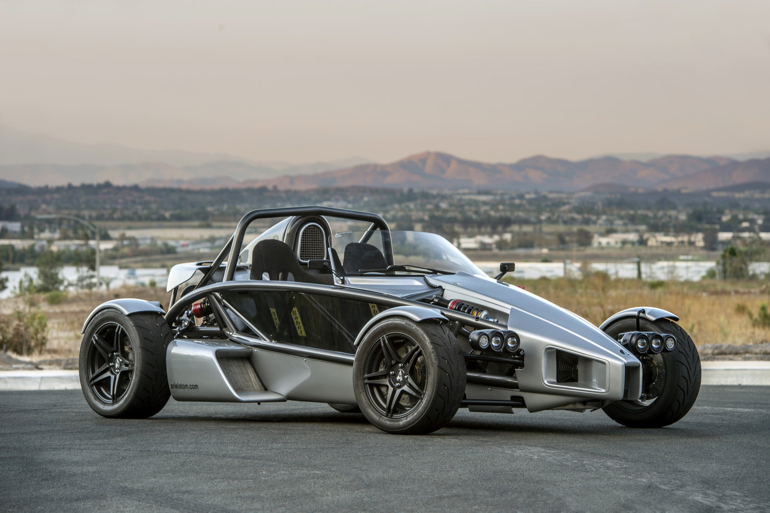 Ariel Atom 3RS open-air sports car parked on pavement with desert mountains in the background.