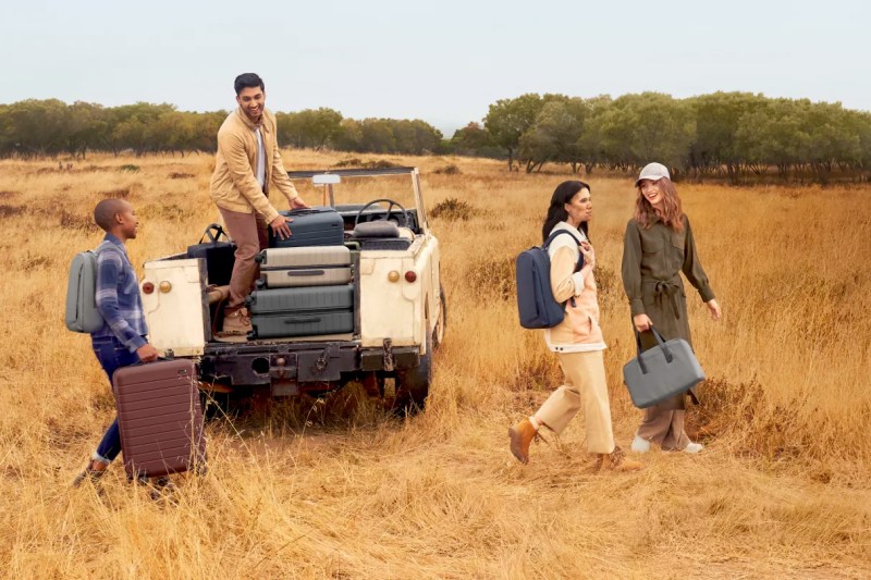 Group of four young people toting luggage in a field of straw standing near a four-wheeler.