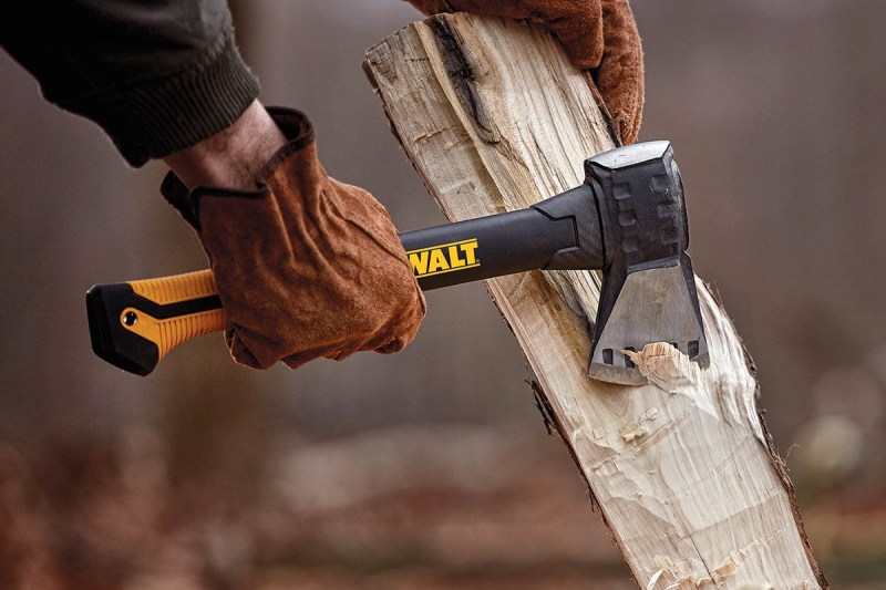 Closeup of a person wearing leather gloves chopping wood with a Dewalt hatchet.