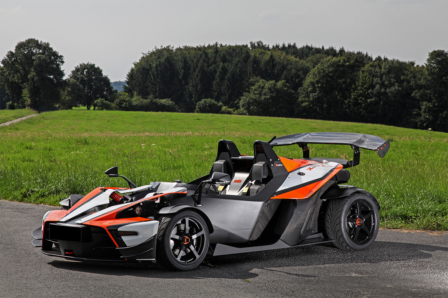 Wimmer-RST KTM X-Bow GT parked on pavement near a green open field.